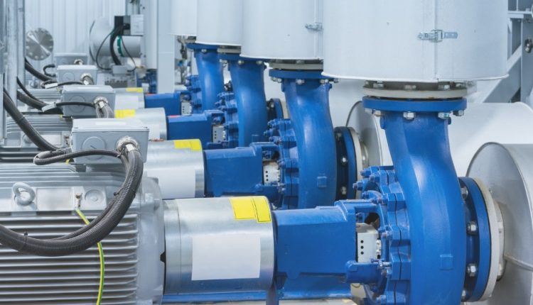 Row of blue industrial pumps connected to electric motors in a mechanical room, with cables and metal piping.