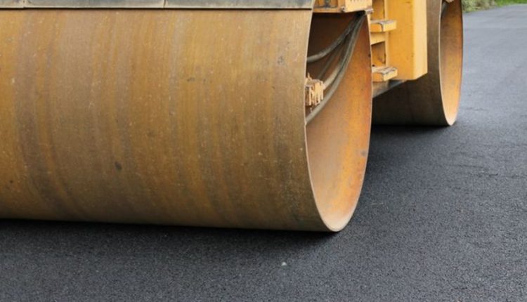 Close-up of a yellow road roller compacting fresh asphalt on a street.